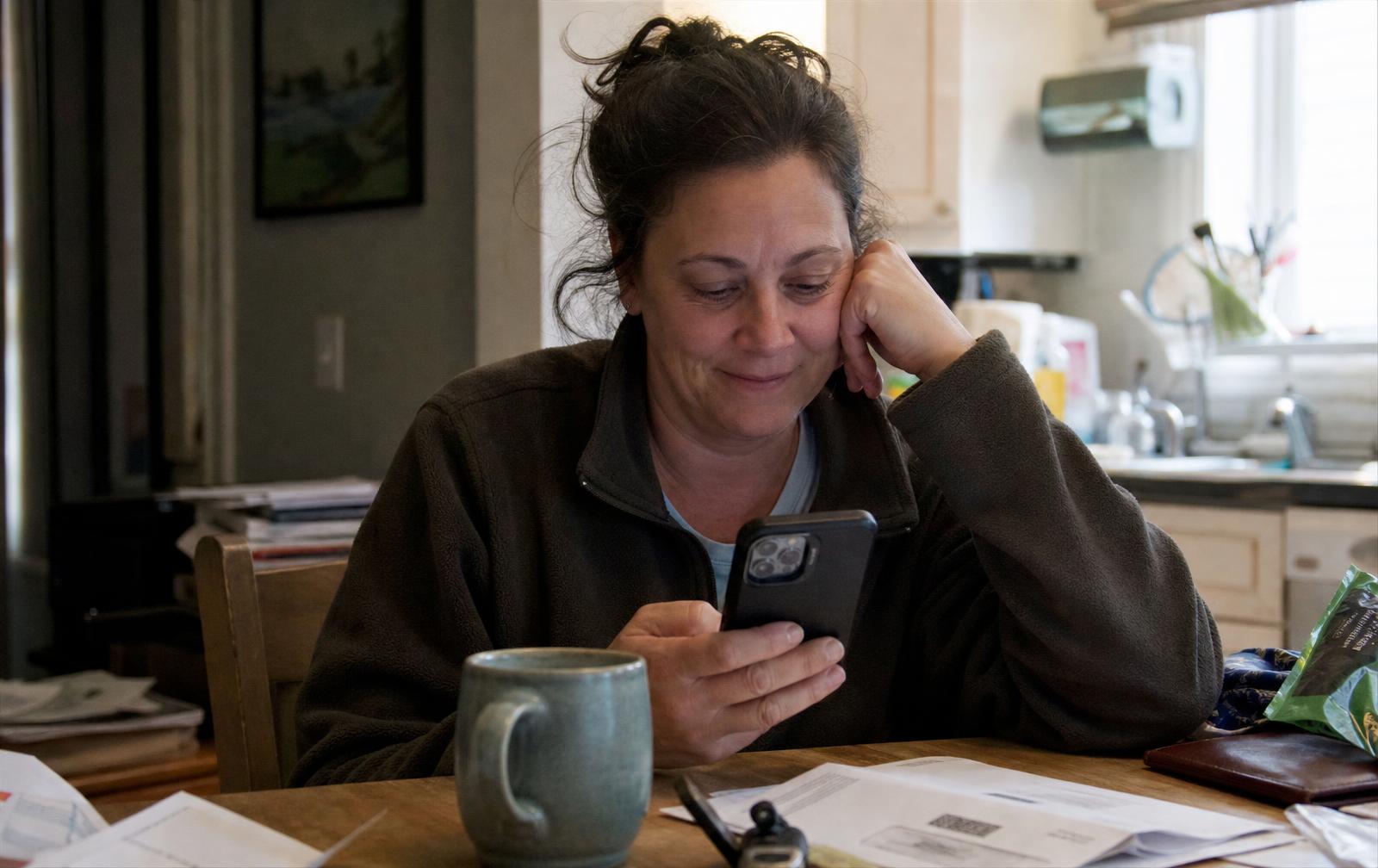 A woman in her fifties at her kitchen table smiling at the recording link that arrived on her phone