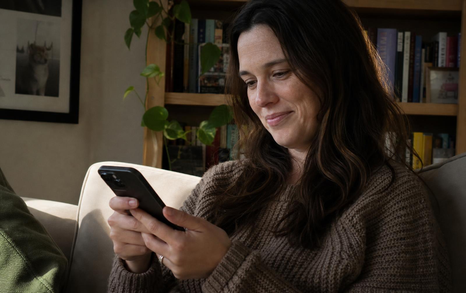 A woman in her thirties on her sofa tapping her phone to play back the video she just recorded